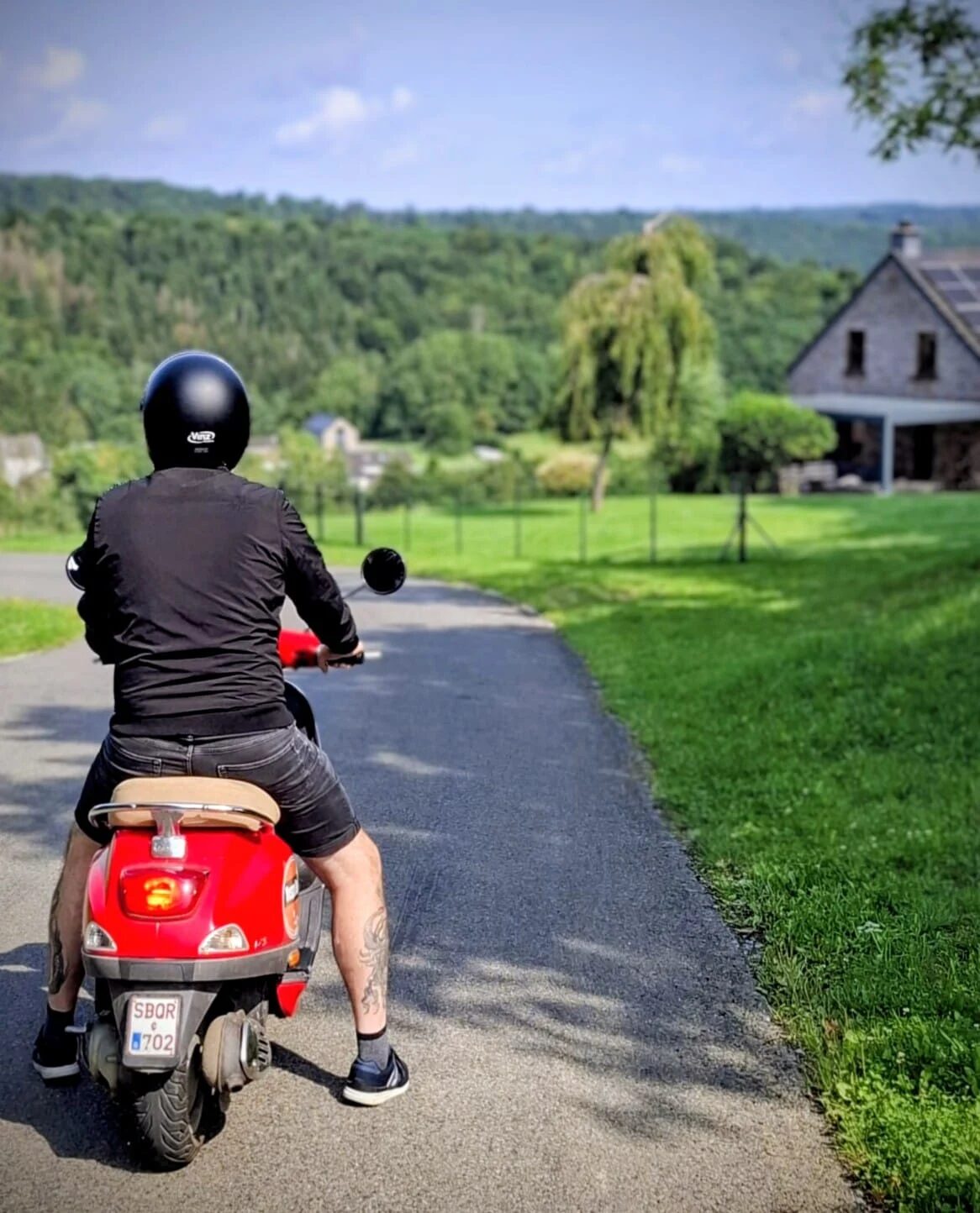 Vespa rijder op een schilderachtige weg door de groene Ardennen